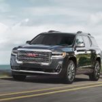A black 2020 GMC Acadia, which wins when comparing the 2020 GMC Acadia vs 2020 Kia Telluride, is driving past a bay.