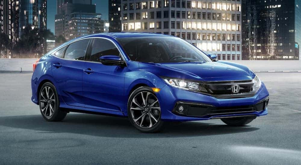 A blue 2020 Honda Civic Sedan Sport is parked in the city in the rain at night.
