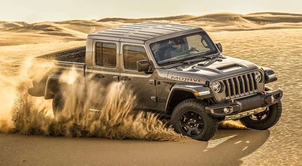 A grey 2020 Jeep Gladiator, which wins when comparing the 2020 Jeep Gladiator vs 2020 Toyota Tacoma, is drifting through desert sand.