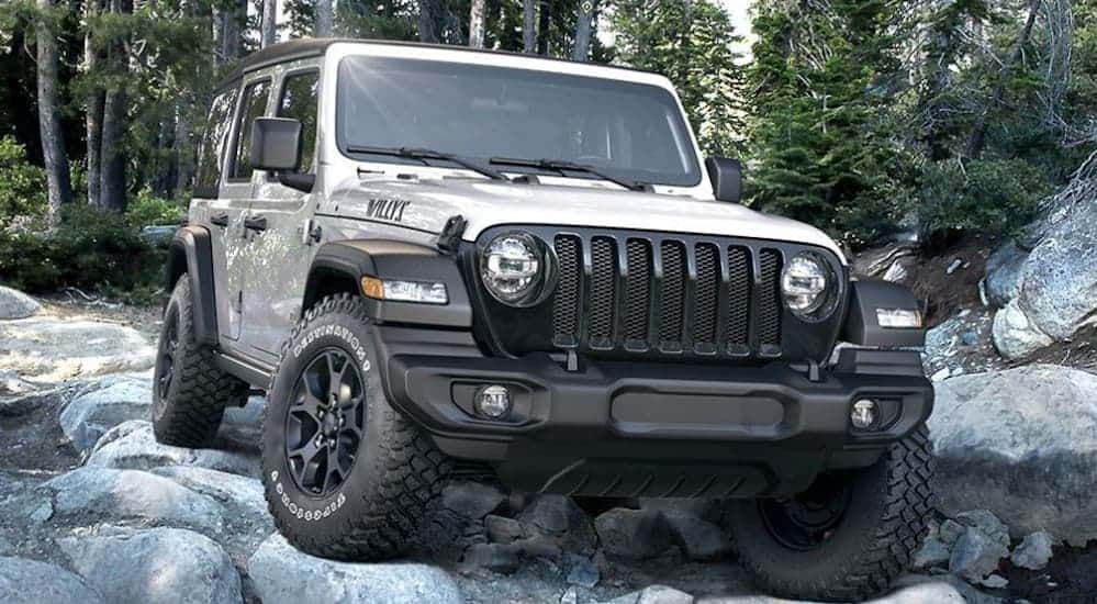 A silver 2020 Jeep Wrangler is rock crawling through the woods.