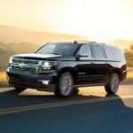 A black 2020 Chevy Suburban is driving with a sunset behind it.