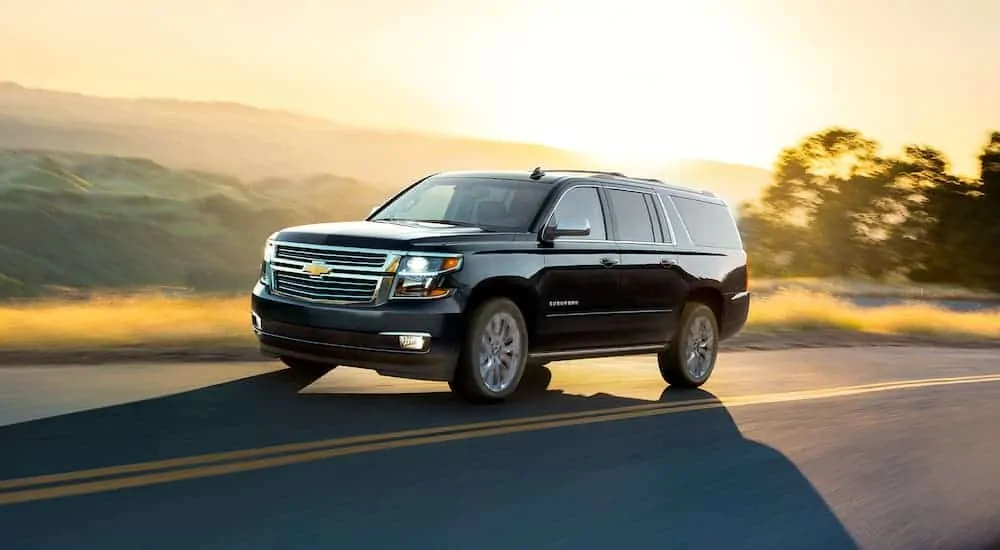 A black 2020 Chevy Suburban is driving with a sunset behind it.