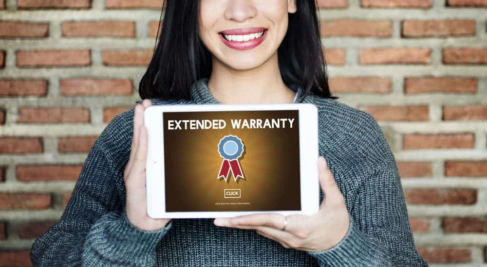 A smiling woman is holding up an iPad that says Extended Warranty on it.