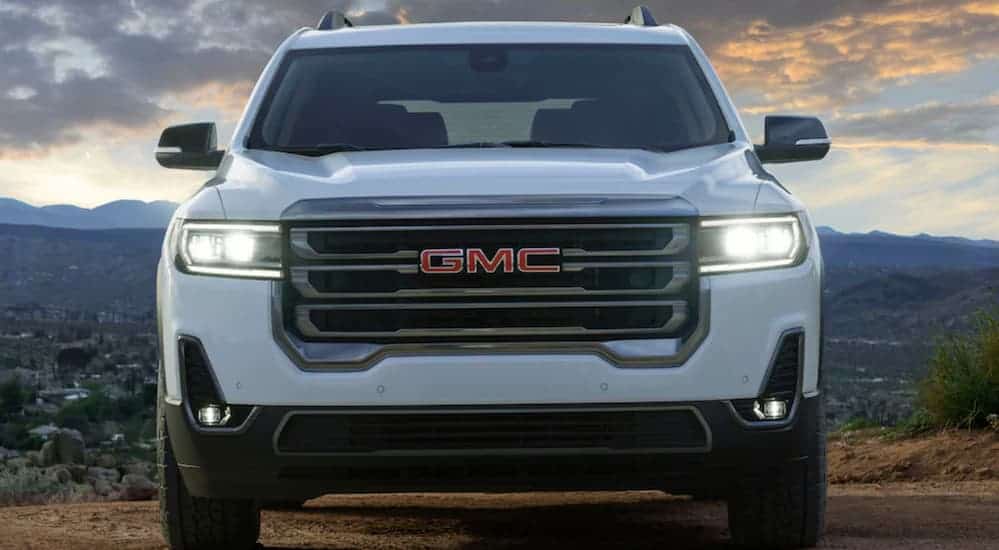 A white 2020 GMC Acadia AT4 is parked, while facing forward, on a dirt trail that's overlooking a city at dusk.