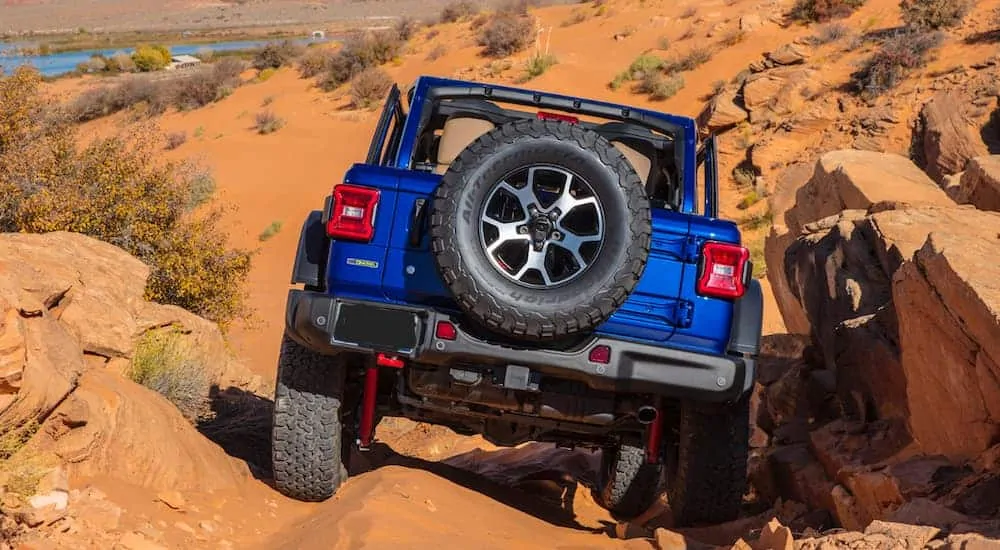 A blue 2020 Jeep Wrangler from the rear is rock crawling down a large rock hill in the desert.