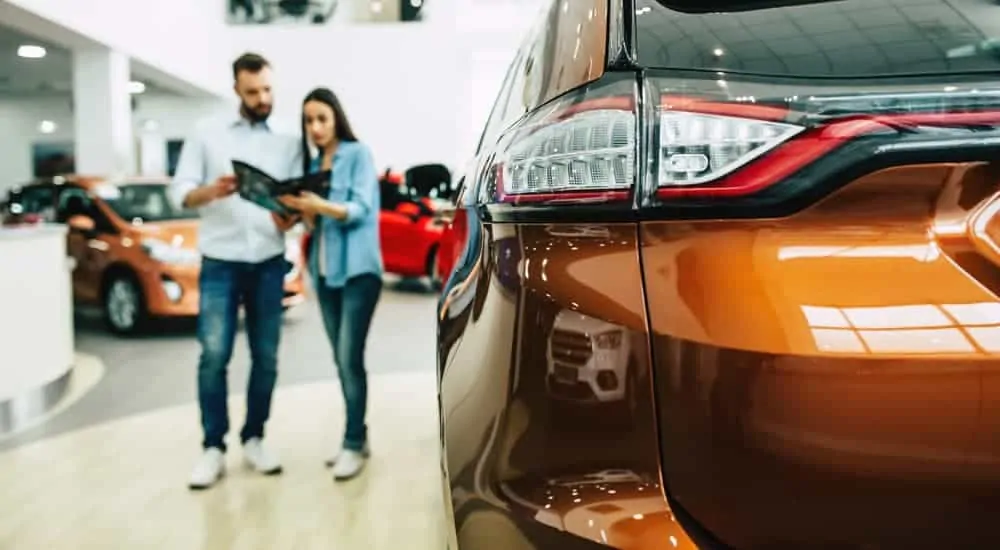 A couple is looking at a book with used cars for sale in Ohio while standing in a dealerships showroom.