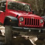 A red 2018 Jeep Wrangler, which is a popular option among used SUVs for sale, is rock crawling through the woods.