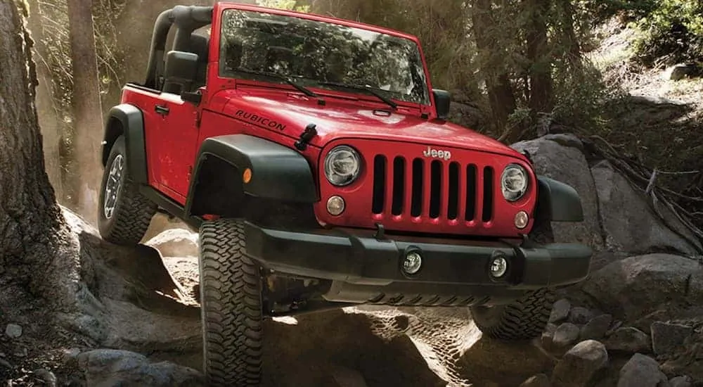 A red 2018 Jeep Wrangler, which is a popular option among used SUVs for sale, is rock crawling through the woods.