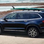 A blue 2020 Honda Pilot is parked at the ocean with a surfboard on the roof rack.