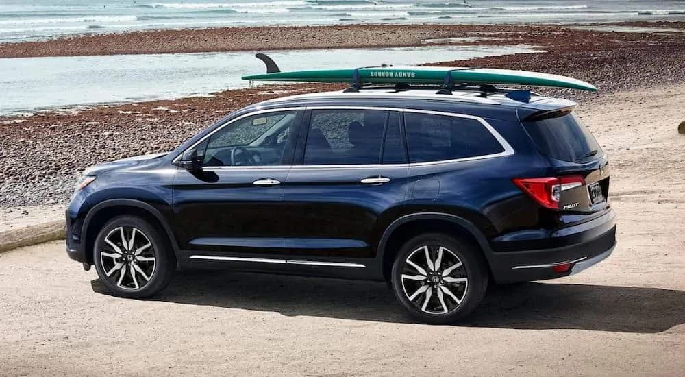 A blue 2020 Honda Pilot is parked at the ocean with a surfboard on the roof rack.