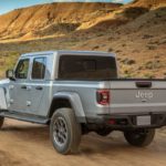 A silver 2020 Jeep Gladiator is driving on a dirt road in the desert.