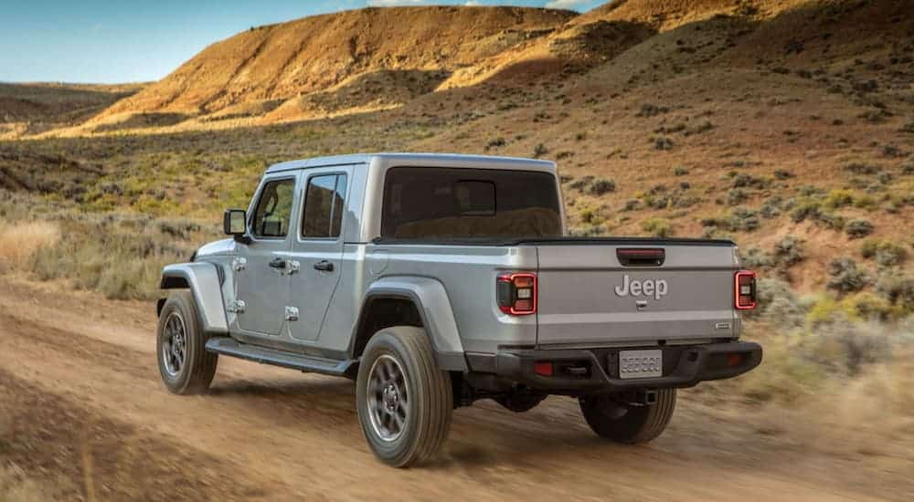 A silver 2020 Jeep Gladiator is driving on a dirt road in the desert.