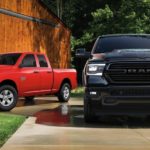 A red 2020 Ram 1500 Classic Express is next to a black 1500 in front of a barn.
