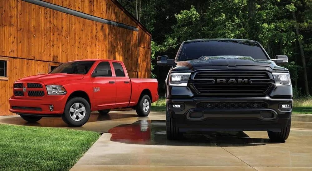 A red 2020 Ram 1500 Classic Express is next to a black 1500 in front of a barn.