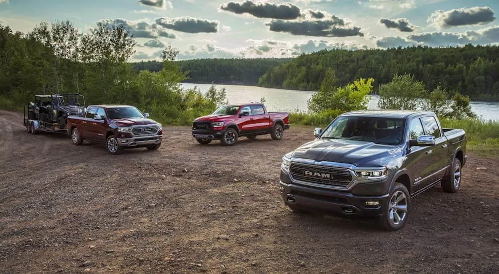 A burgundy, a red, and a dark grey 2020 Ram 1500 are parked in front of a lake.