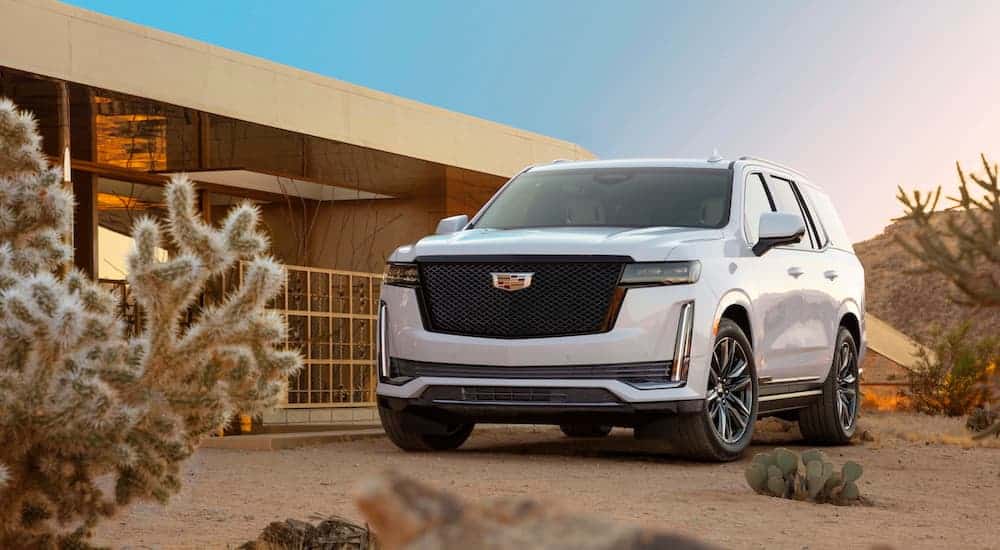 A white 2021 Cadillac Escalade is parked in front of a modern house in a desert area.