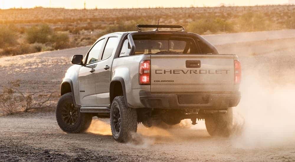 A tan 2021 Chevy Colorado ZR2 is shown from the rear on a dusty dirt road.