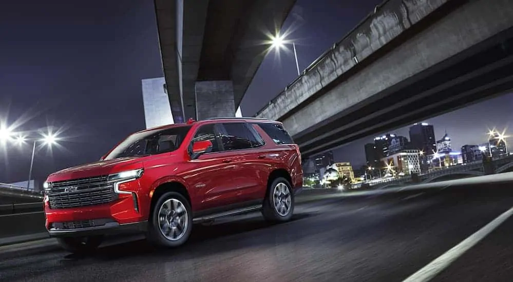 A red 2021 Chevy Tahoe is driving on a highway with a night time city skyline in the distance.