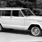 The ancestor of the 2021 Jeep Wagoneer, a white 1966 Wagoneer is parked in a lot.