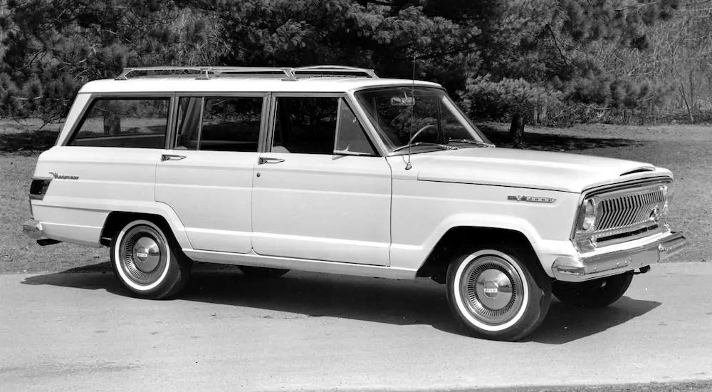 The ancestor of the 2021 Jeep Wagoneer, a white 1966 Wagoneer is parked in a lot.