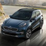 A blue 2020 Kia Sportage, assumed to be similar to the 2021, is driving away from a city.