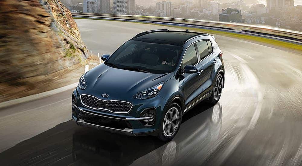 A blue 2020 Kia Sportage, assumed to be similar to the 2021, is driving away from a city.