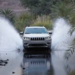 A silver 2020 Jeep Cherokee from the front, splashing through a river