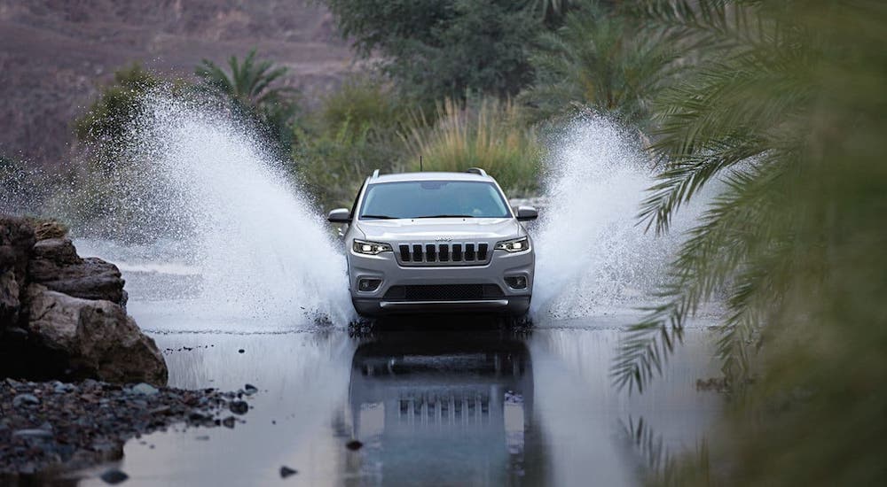 A silver 2020 Jeep Cherokee from the front, splashing through a river