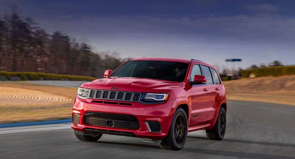 A red 2020 Jeep Grand Cherokee is driving on a racetrack with a dark sky.