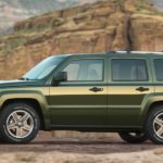 A green 2007 Jeep Patriot is parked in front of desert rocks.