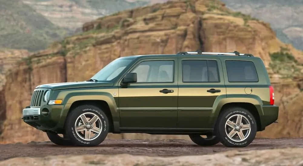 A green 2007 Jeep Patriot is parked in front of desert rocks.