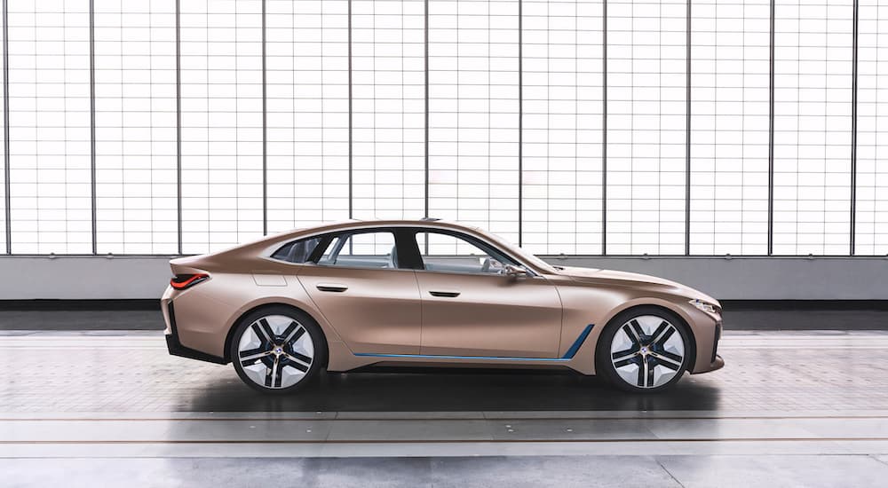 A side view of a beige 2021 BMW i4 is shown in front of windows, which will have a long wait before it is a used car for sale.