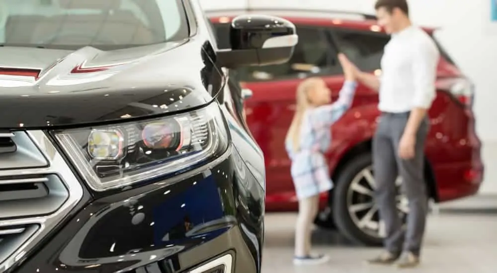 A father and daughter are high fiving next to used cars near me for sale.