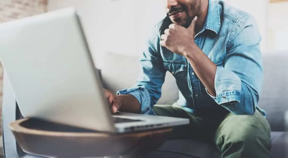 A man is researching used cars near him on a laptop.