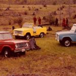 A red, yellow, and a blue 1969 Ford Bronco are parked off-road.