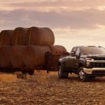 A black 2020 Chevy Silverado 3500HD is towing a trailer with hay bales in a field.