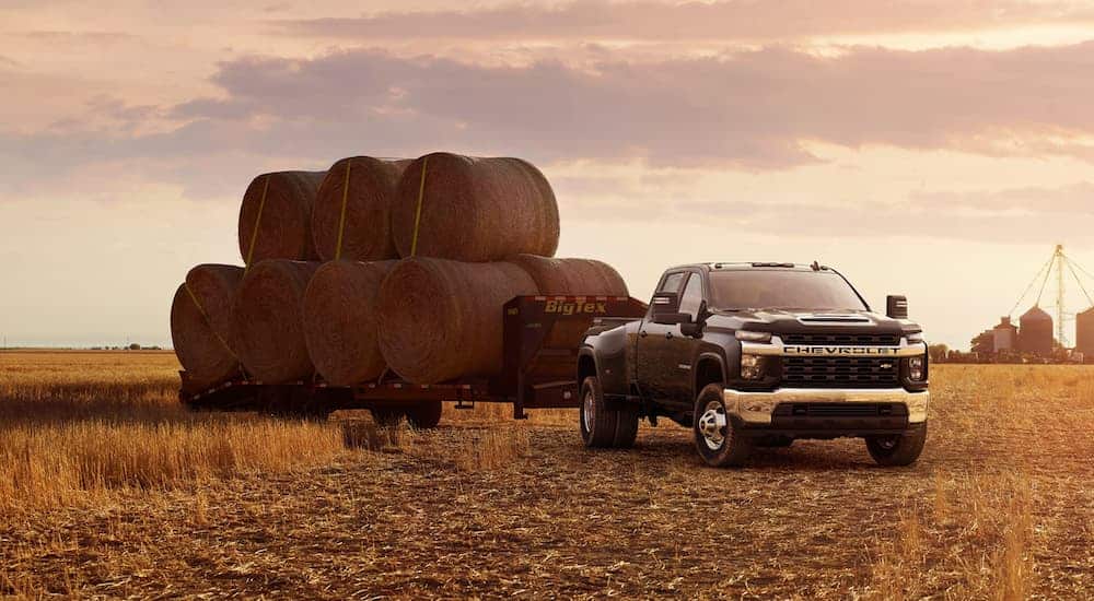 A black 2020 Chevy Silverado 3500HD is towing a trailer with hay bales in a field.