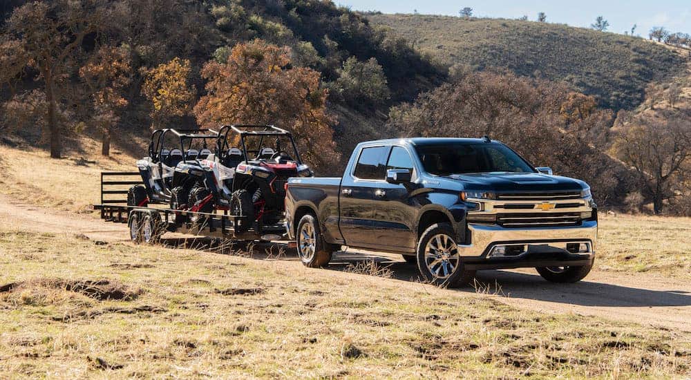 A dark grey 2020 Chevy Silverado is towing side by sides on a dirt road.