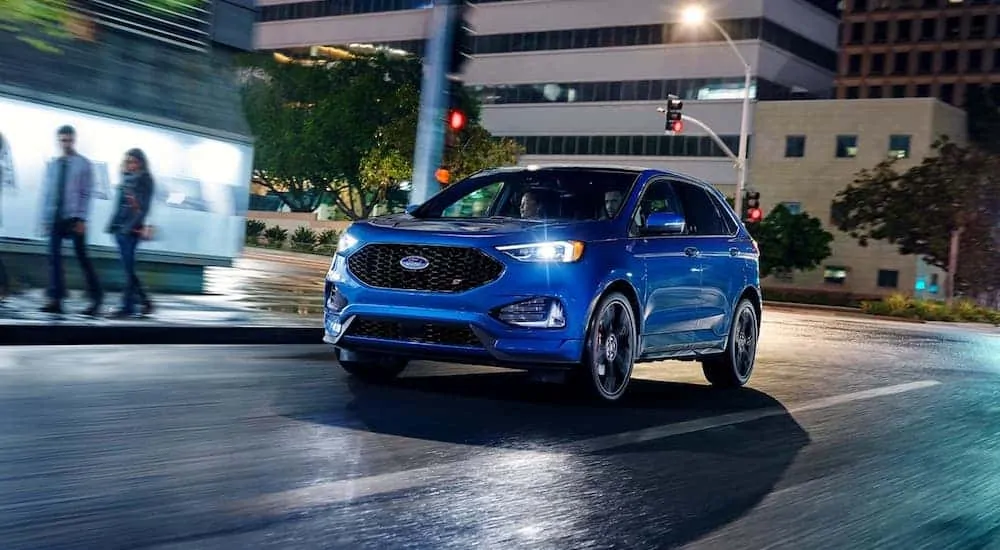 A blue 2020 Ford Edge is driving on a city street at night.