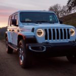 A white 2020 Jeep Wrangler is driving on a rural road at dusk.