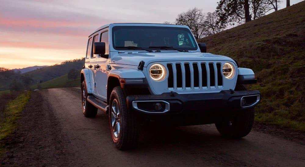 A white 2020 Jeep Wrangler is driving on a rural road at dusk.