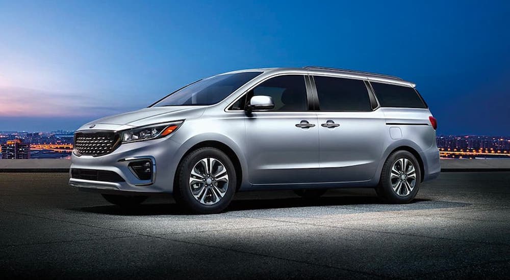 A silver 2020 Kia Sedona is parked in an empty lot at night.