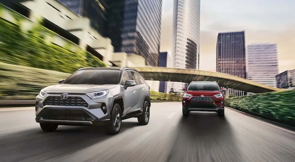 A red 2020 Toyota RAV4 is driving behind a silver one on a multi-lane city street.