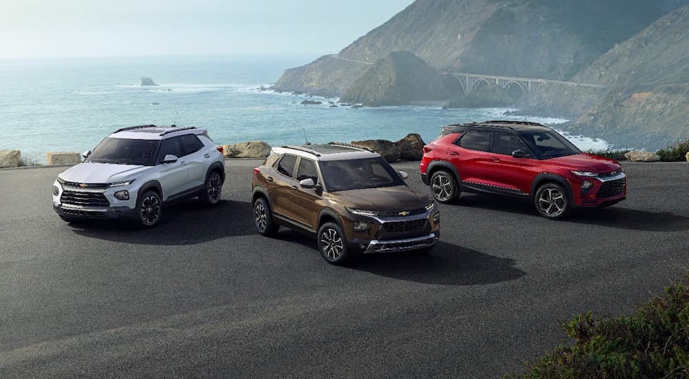 Three 2021 Chevy Trailblazers, one white, one red, one brown, are parked in front of a cliff and the ocean.