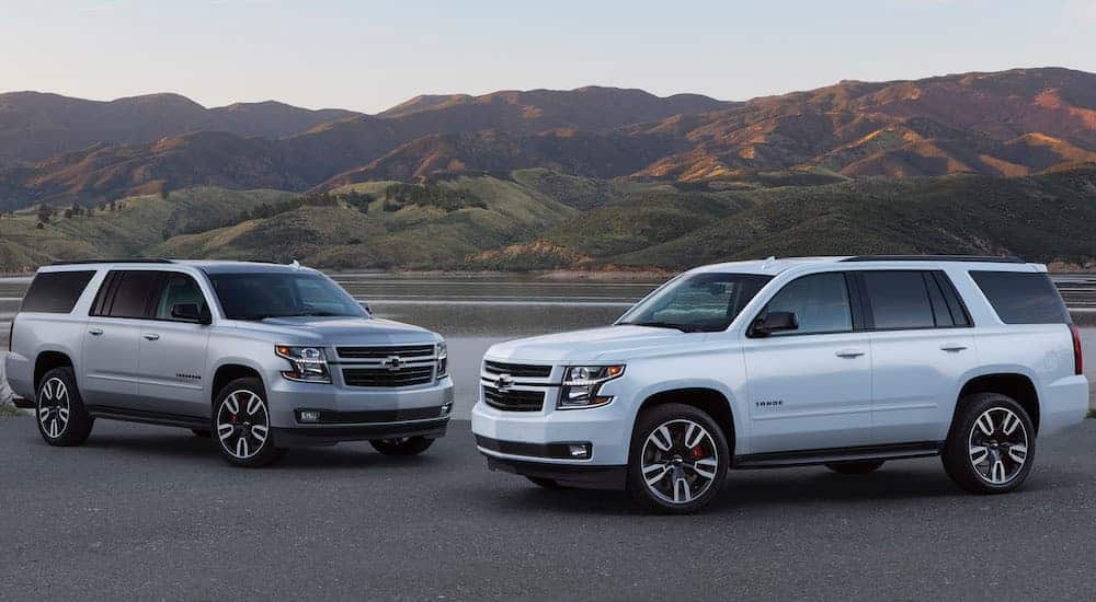 A white 2020 Chevy Tahoe is parked next to a silver 2020 Chevy Suburban with mountains in the distance.