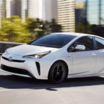 A white 2020 Toyota Prius is driving out of a city after leaving a Toyota dealer near me.