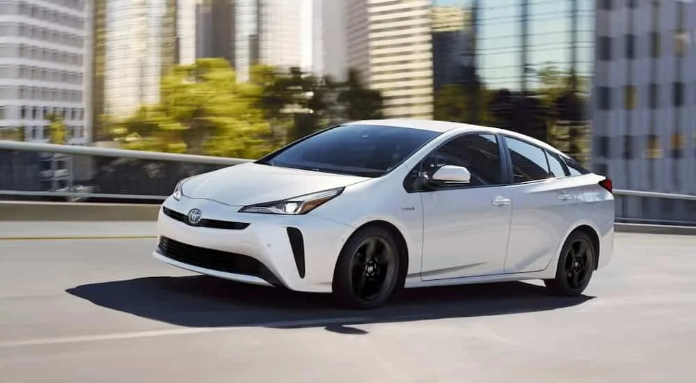 A white 2020 Toyota Prius is driving out of a city after leaving a Toyota dealer near me.