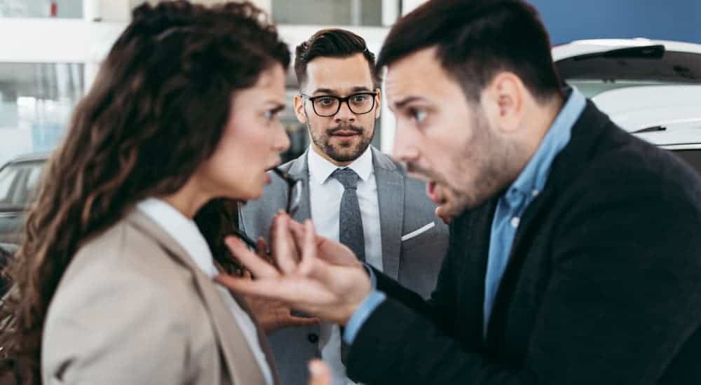 A man and woman are fighting in front of a concerned man at a used car dealership near me.