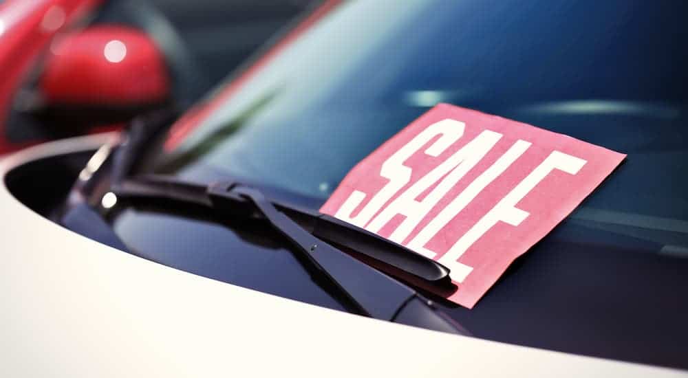 A Sale sign is sitting on a car windshield at a used car dealership.