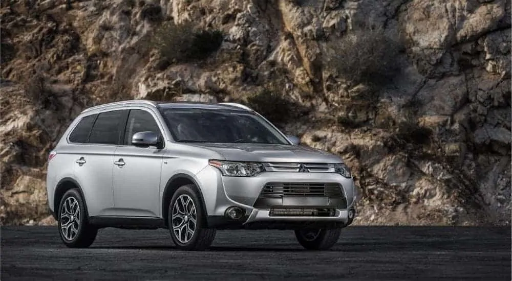A silver 2015 Mitsubishi Outlander is parked in front of a rock face.